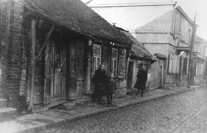 A woman and child pose on the street in front of a wooden house in the Kovno ghetto